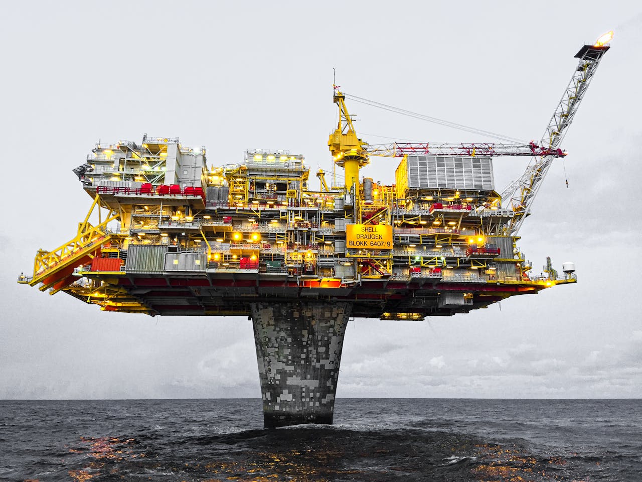 A well-lit offshore oil platform against a cloudy sky in Norways waters.